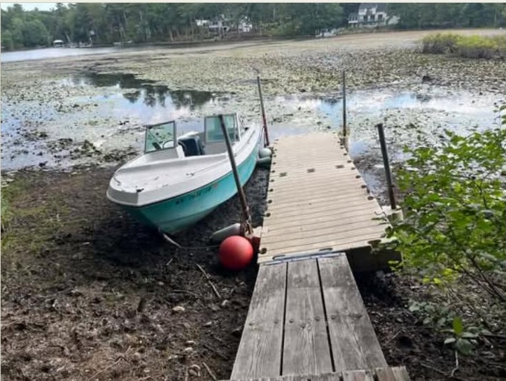A boat and wooden dock stranded on dry lakebed mud at Woodvue Road, Windham, New Hampshire